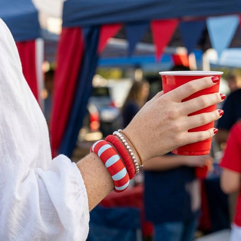 woman wearing a powder blue and red Butter Republic bracelet, holding a red plastic cup at an outdoor tailgate
