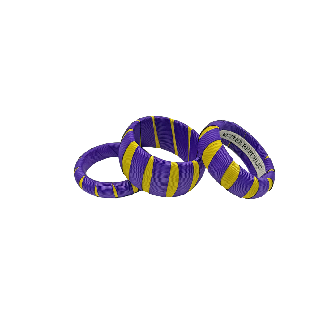three multi-sized purple and yellow Butter Republic bracelets with a brand label on the interior of the bracelets