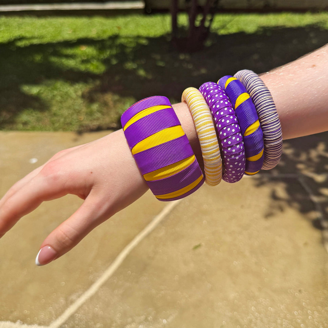 Woman wearing multiple purple and gold Butter Republic bracelets on a concrete surface with grass and trees in the background