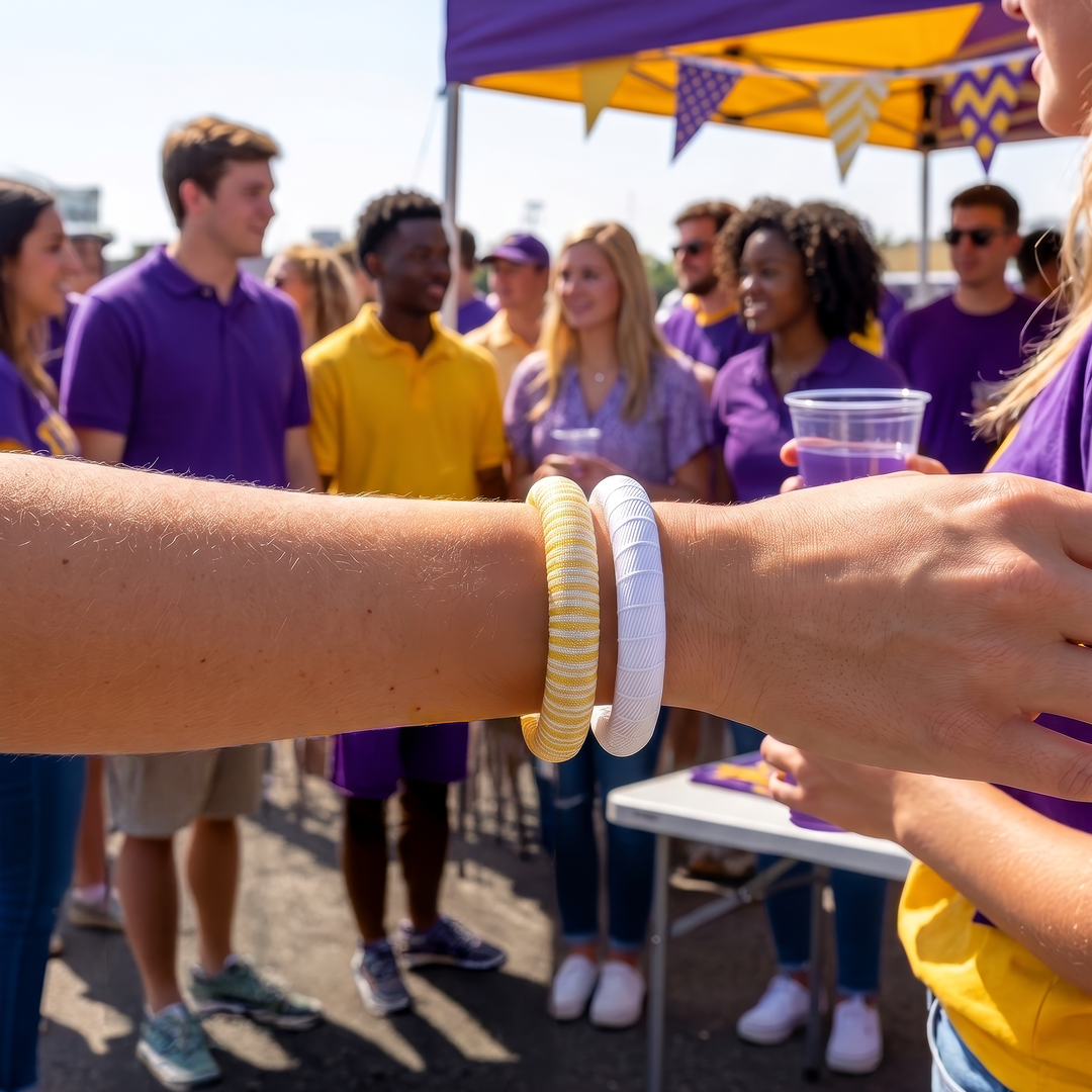 A woman wearing two yellow and white Butter Republic bracelets, standing in a group of people at an outdoor tailgate event with a purple and yellow tent.