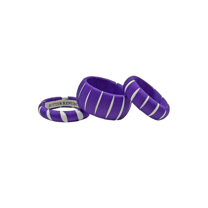 three multi-sized purple and white Butter Republic bracelets with a brand label on the interior of one of the bracelets