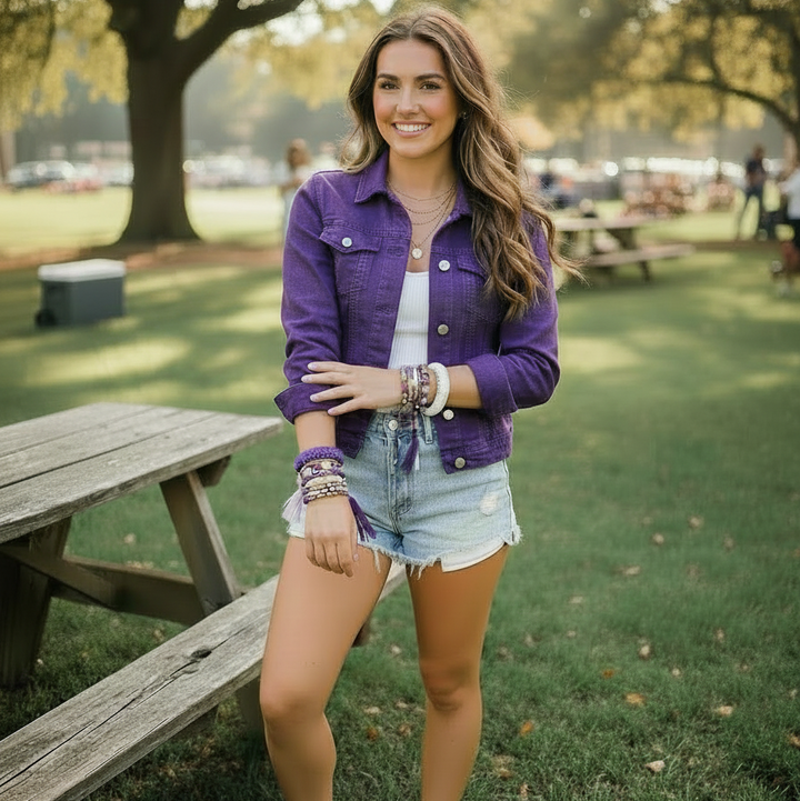 woman in a purple jacket standing in a park with picnic tables and trees, wearing purple and white Butter Republic bracelets
