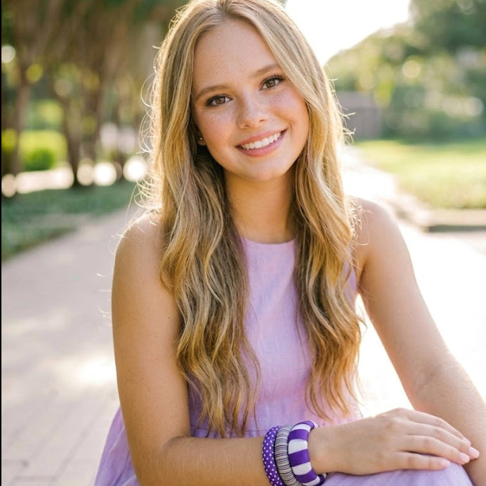 young woman in a lavender dress wearing three purple and white Butter Republic bracelets, sitting outdoors with a blurred background