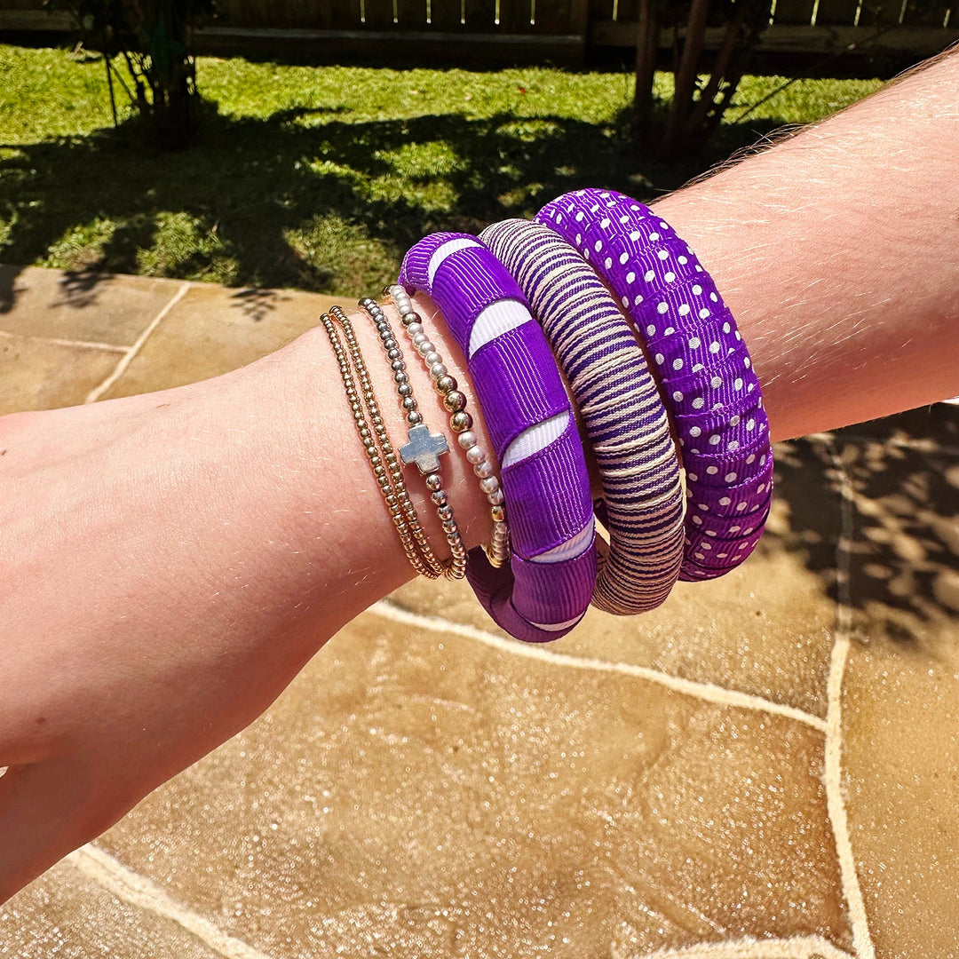 Wrist with multiple purple and white Butter Republicn bracelets i