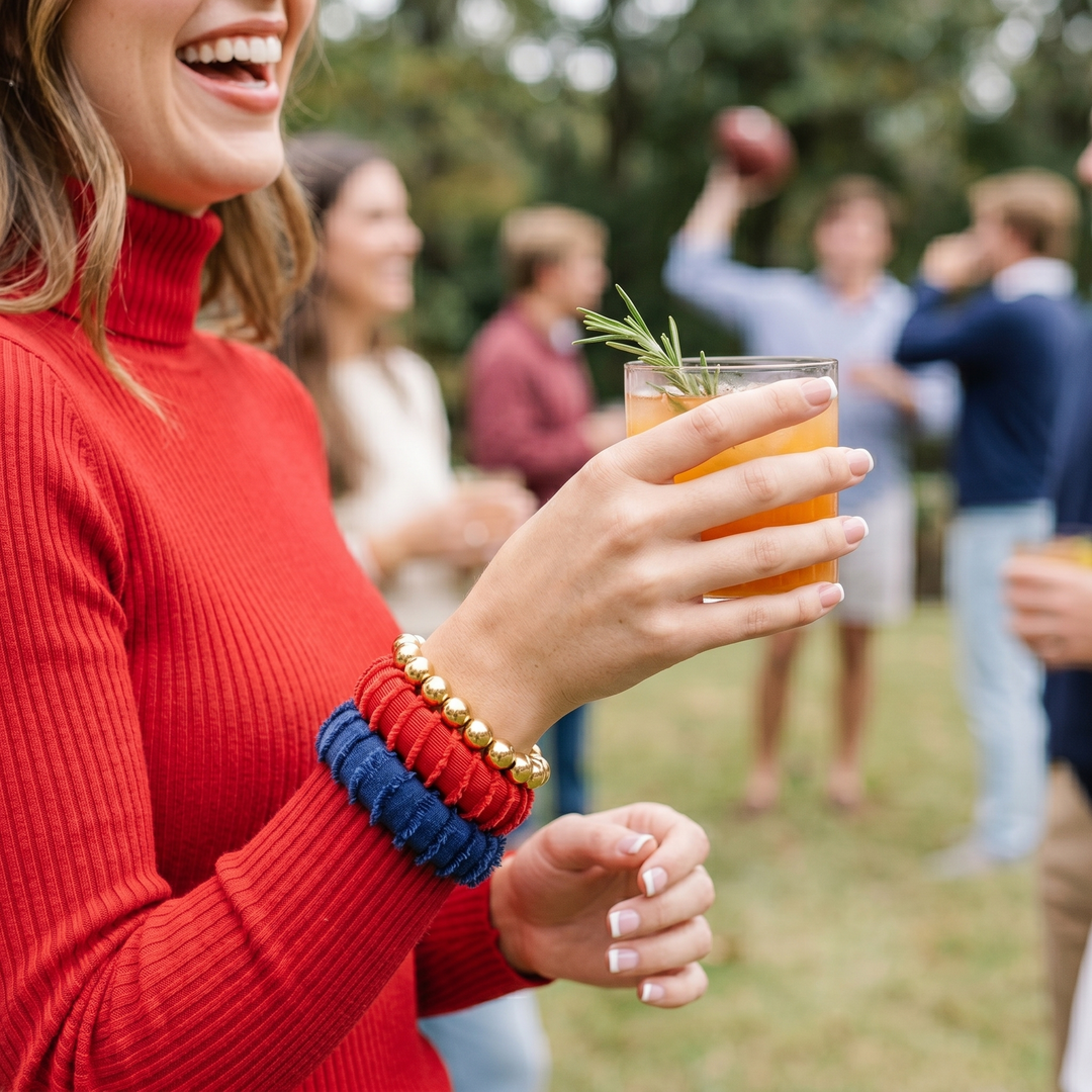 Woman in red sweater, wearing frayed edge Butter Republic bracelets, holding a cocktail with friends in the background