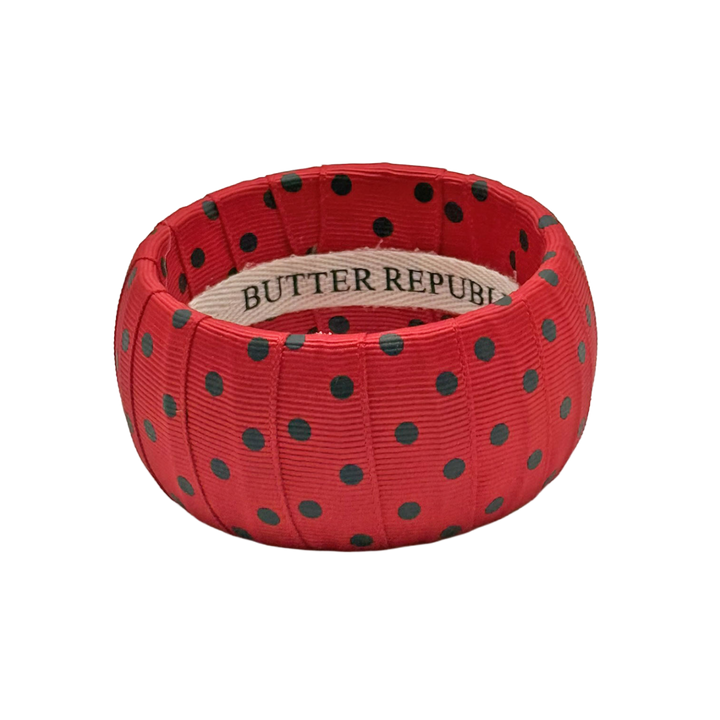red bracelet with black polka dots with a Butter Republic brand label on the interior of the bracelet