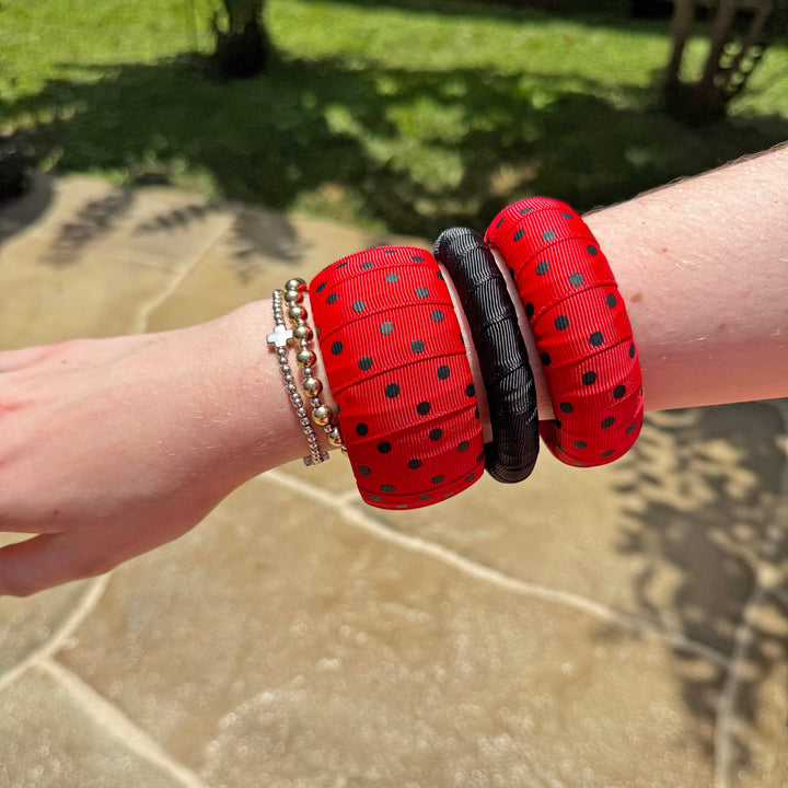 Woman wearing red polka dot Butter Republic bracelets with a blurred outdoor background