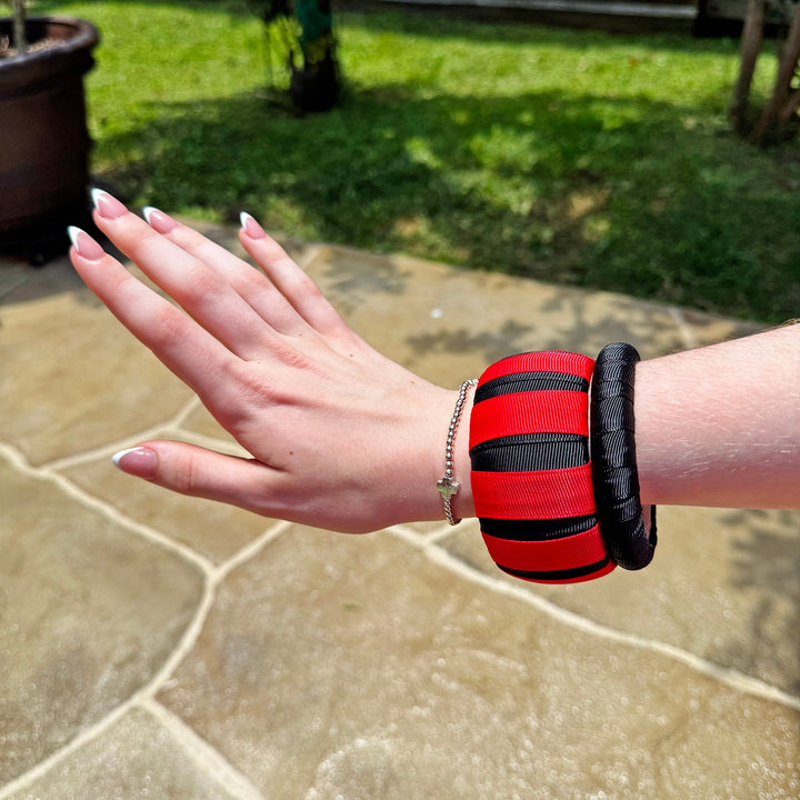 Woman wearing a red and black Butter Republic bracelet on a stone patio with grass and plants in the background