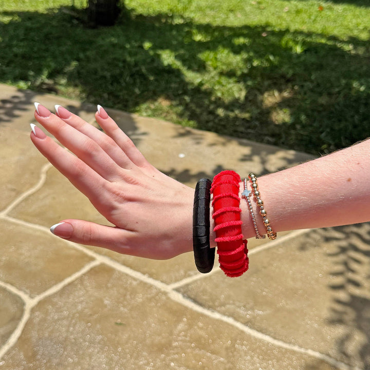Woman wearing red and black Butter Republic bracelets on a patio with grass in the background