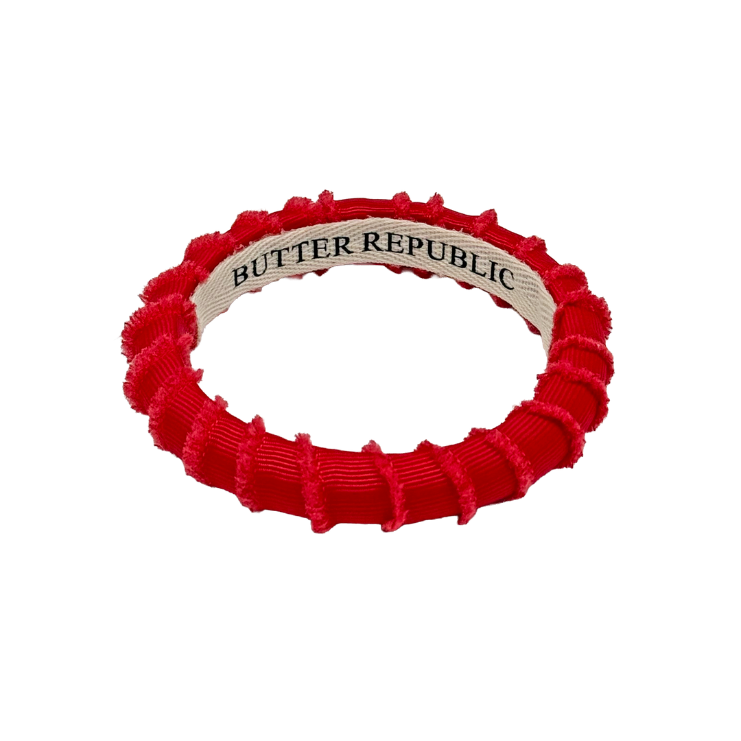Red 'Butter Republic' frayed edge bracelet with a branding llon a white backg