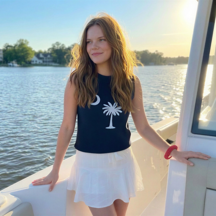 a woman wearing a red and white Butter Republic bracelet in a South Carolina state flag sweater, standing on a boat by a waterfront with a scenic background