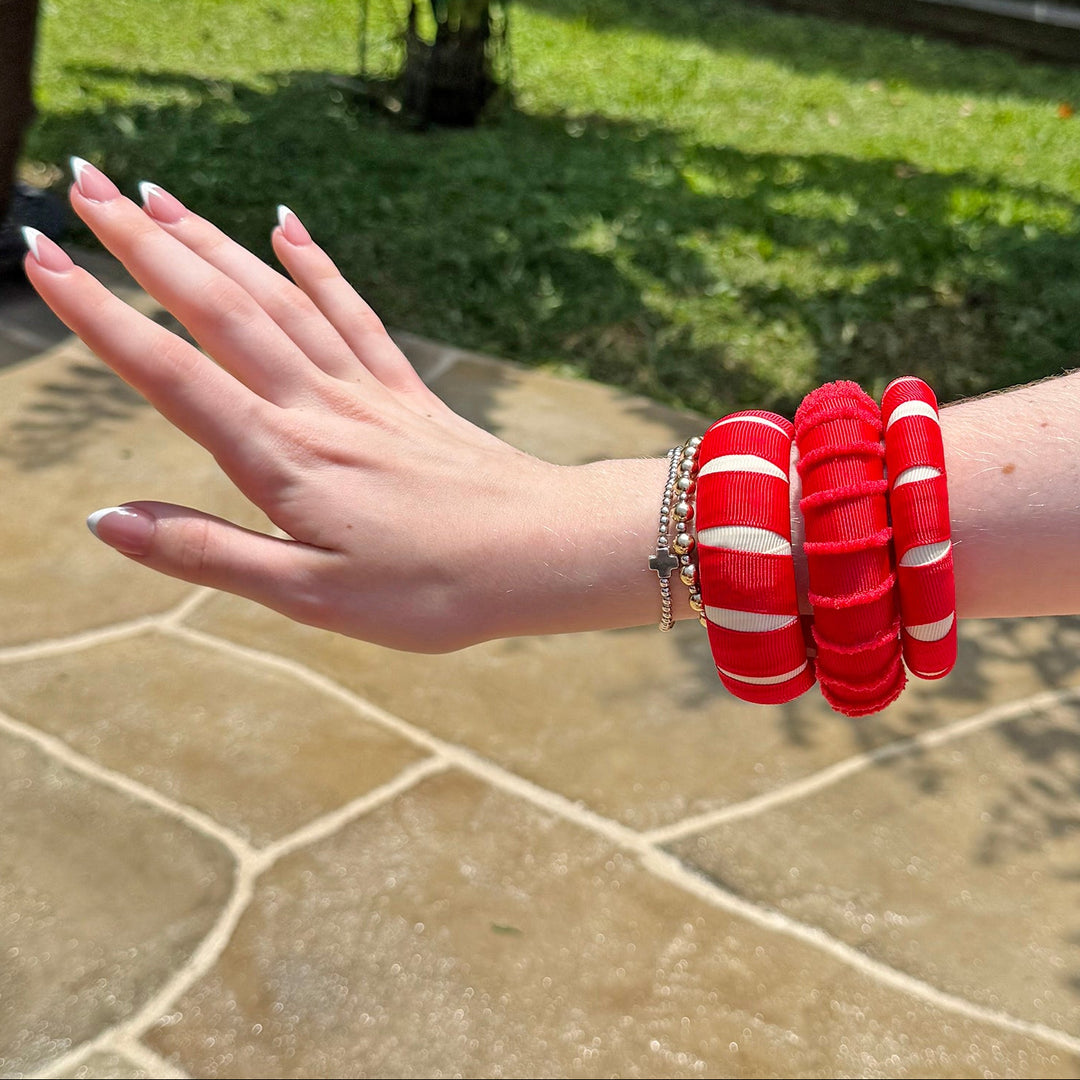 Woman wearing multiple red Butter Republic bracelets on a stone patio with greenery in the background