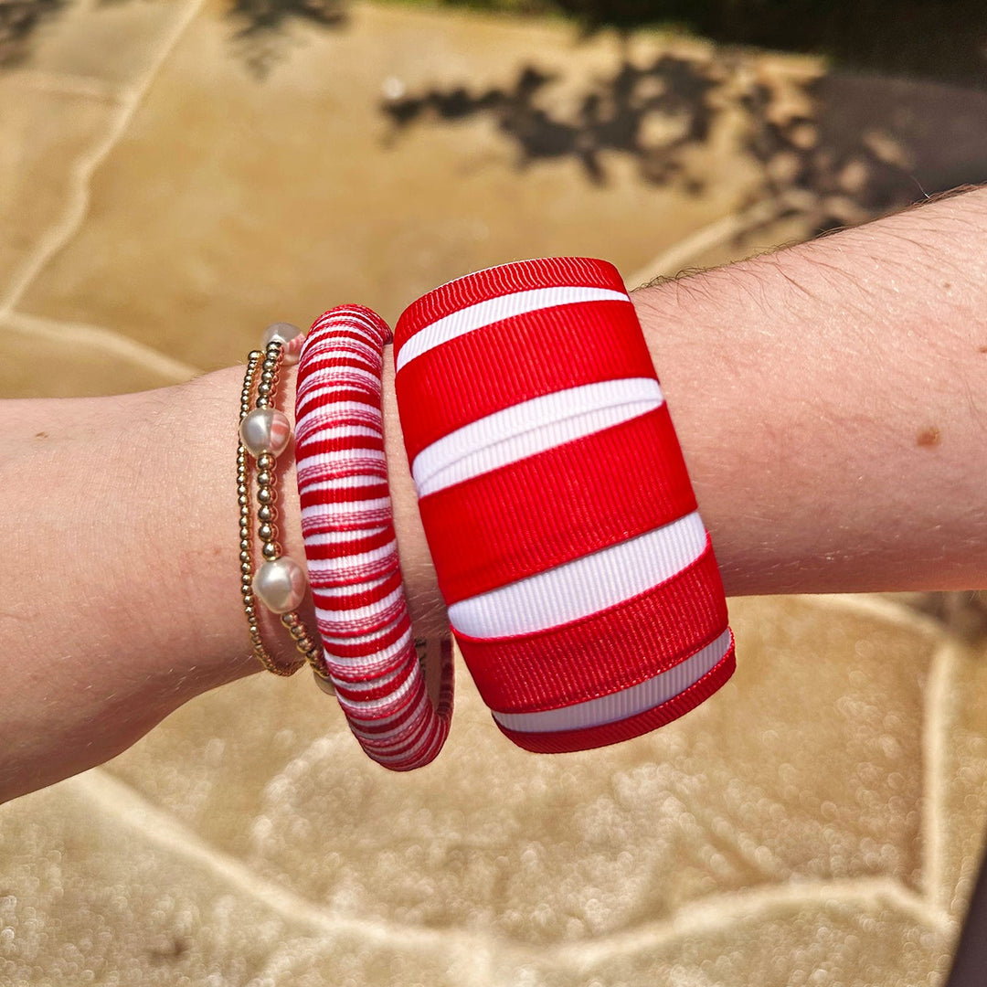 Red and white Butter Republic bracelets on a wrist with a blurred natural background