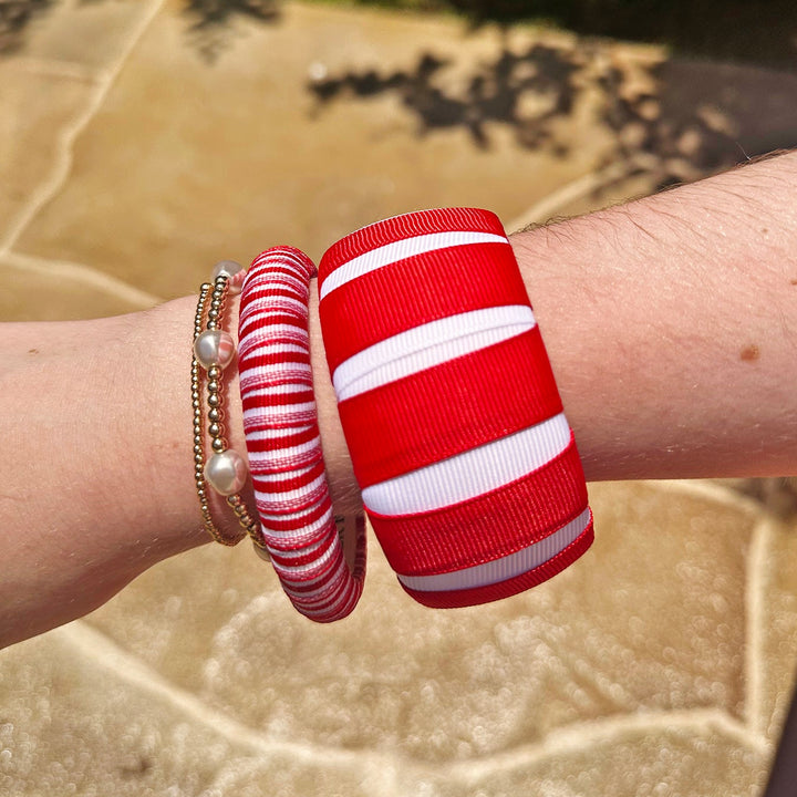 Red and white Butter Republic bracelets on a wrist with a blurred natural background