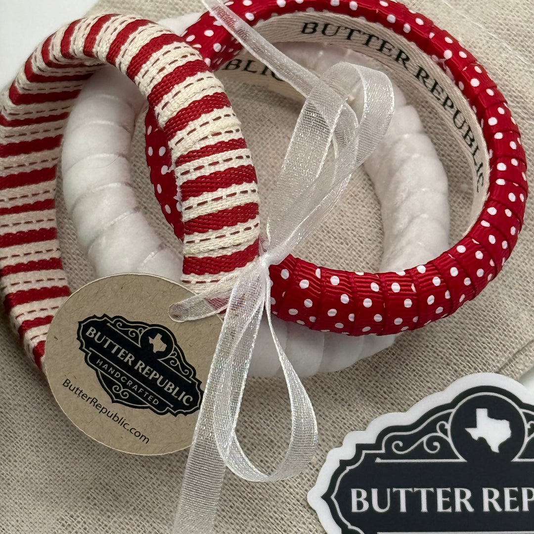 set of three red and white Butter Republic bracelets with a white organza ribbon/bow  securing them together on a beige fabric background