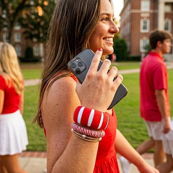 Woman in a red dress wearing Butter Republic bracelets and holding a phone outdoors with buildings and people in the background