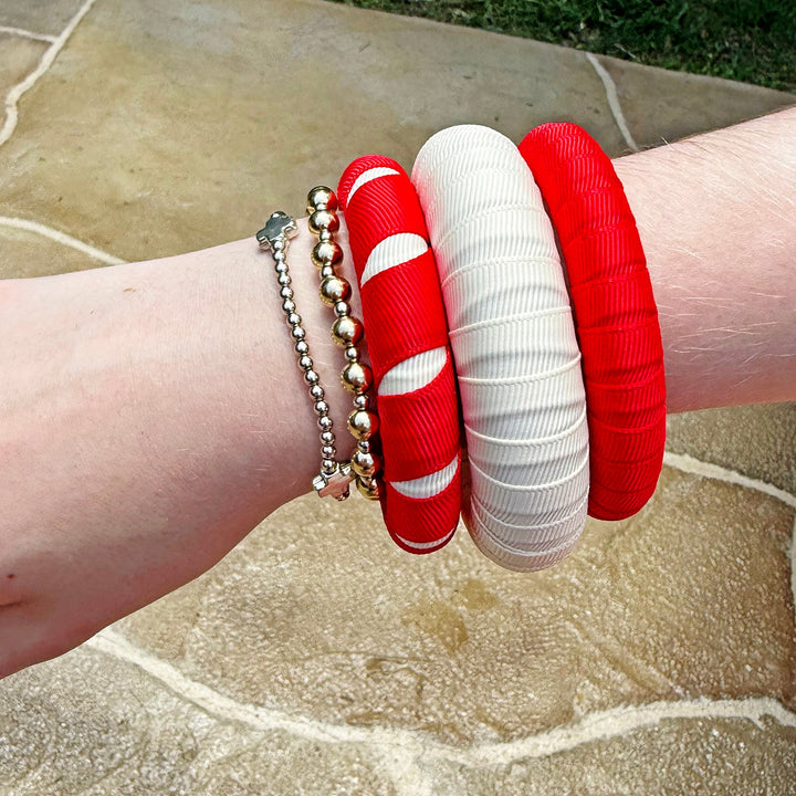 Wrist wearing three red and white Butter Republic bracelets on a stone surface