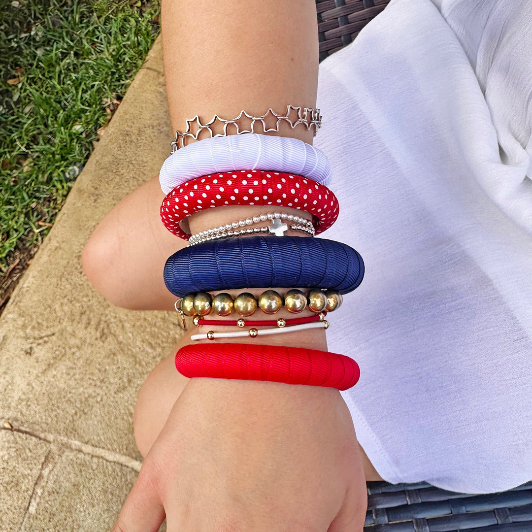 Woman wearing multiple colorful red, white, and blue Butter Republic bracelets on a blurred outdoor background