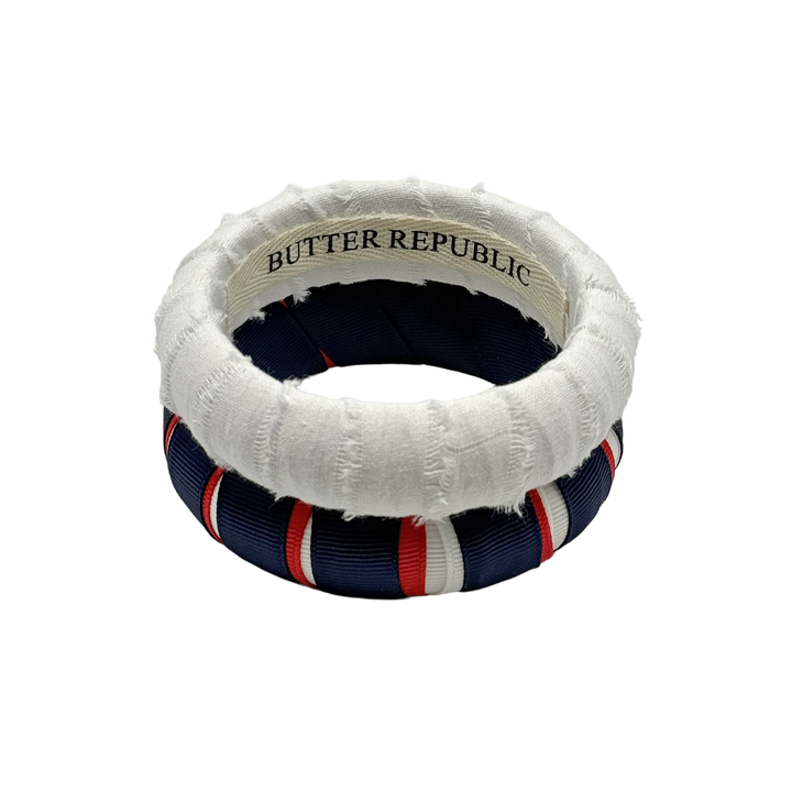 red, white, and navy blue striped Butter Republic bracelet and a white frayed Butter Republic bracelet with a logo brand label on the interior of the bracelet