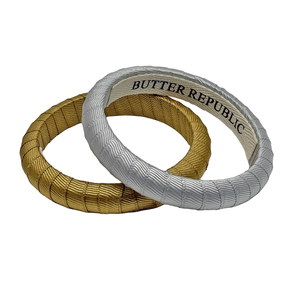 two Butter Republic bracelets, one gold bracelet and one silver Butter Republic bracelet with a logo brand label on the interior of the braceletor