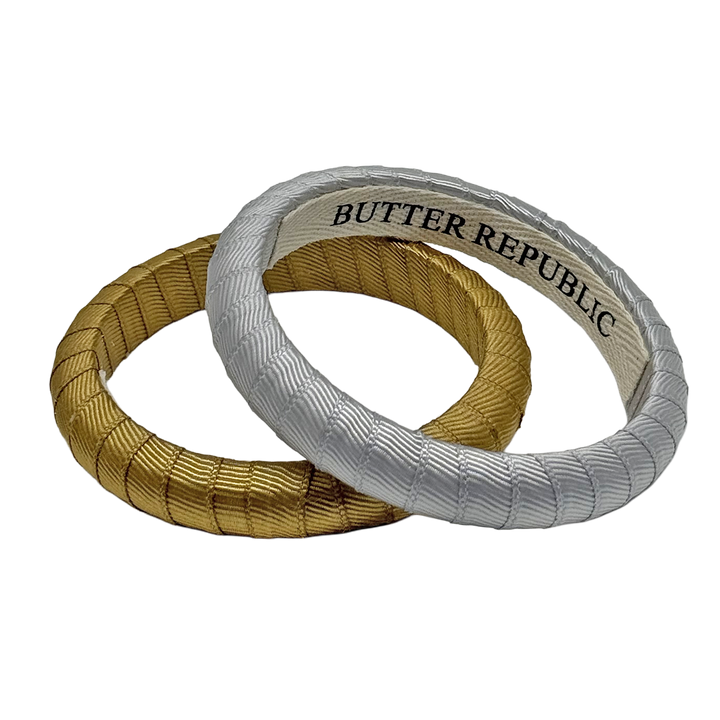 two Butter Republic bracelets, one gold bracelet and one silver Butter Republic bracelet with a logo brand label on the interior of the braceletor