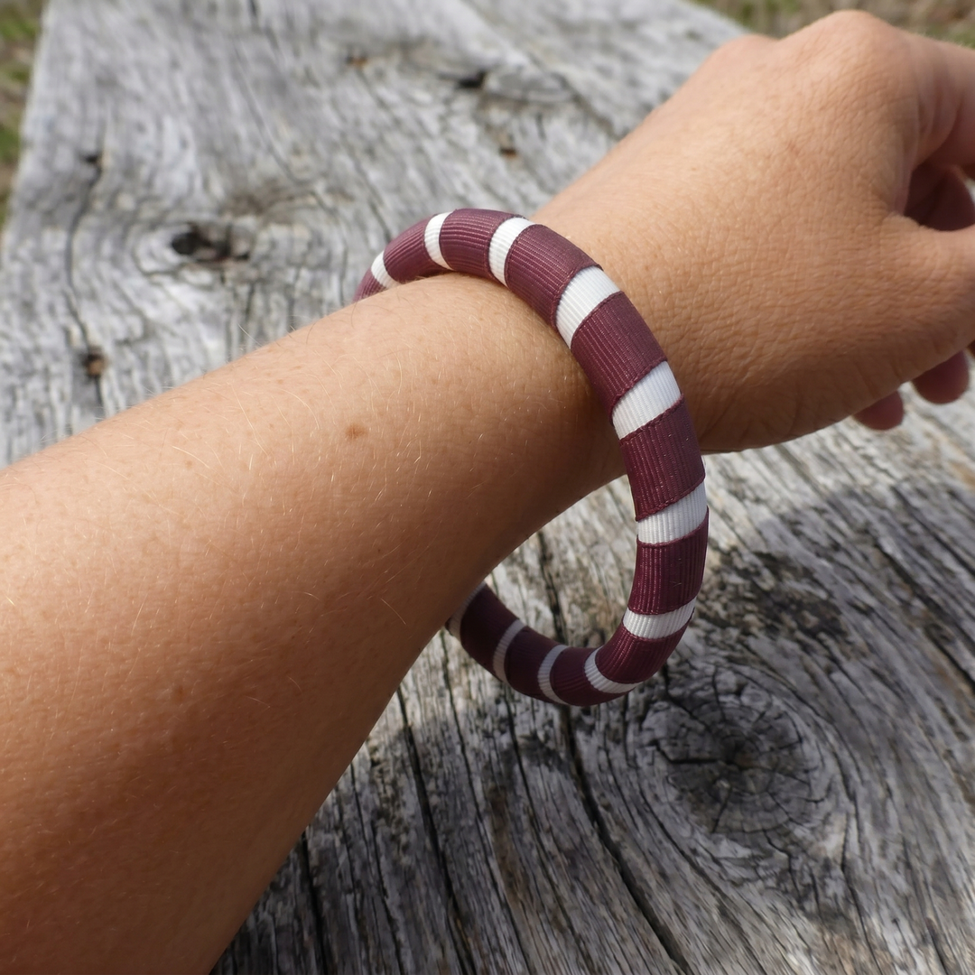 maroon and white striped Butter Republic bracelet that fits too large/loosely on a woman's wrist on a wooden surface