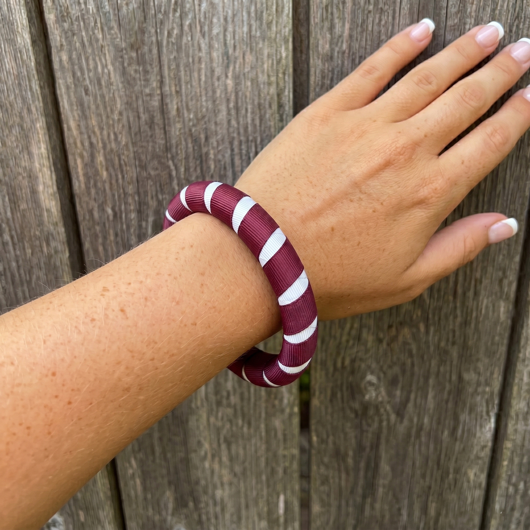 maroon and white striped Butter Republic bracelet that's fits well on a woman's wrist on a wooden surface