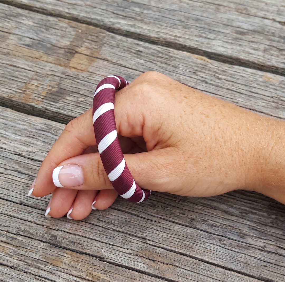maroon and white striped Butter Republic bracelet that fits too small/tightly on a woman's wrist on a wooden surface