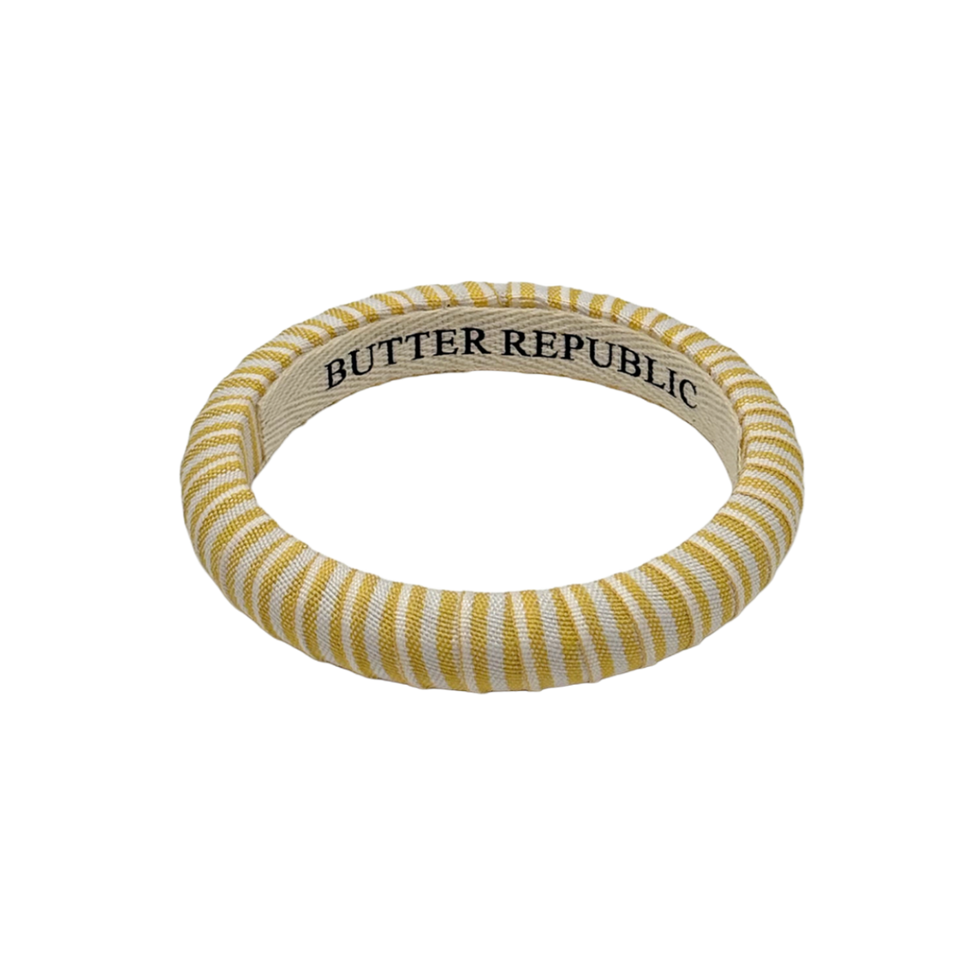 yellow and white striped Butter Republic bracelet with logo brand label visible on the interior of the bracelet