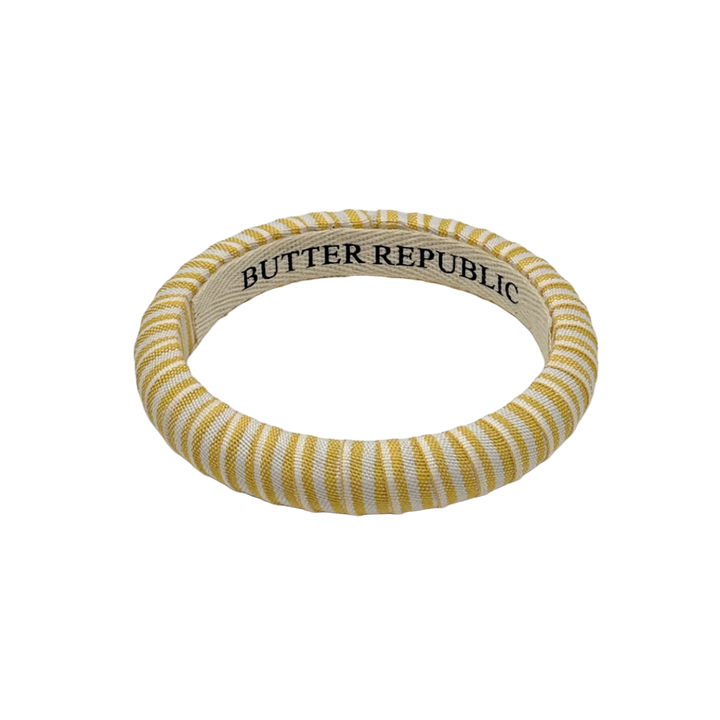 yellow and white striped Butter Republic bracelet with logo brand label visible on the interior of the bracelet