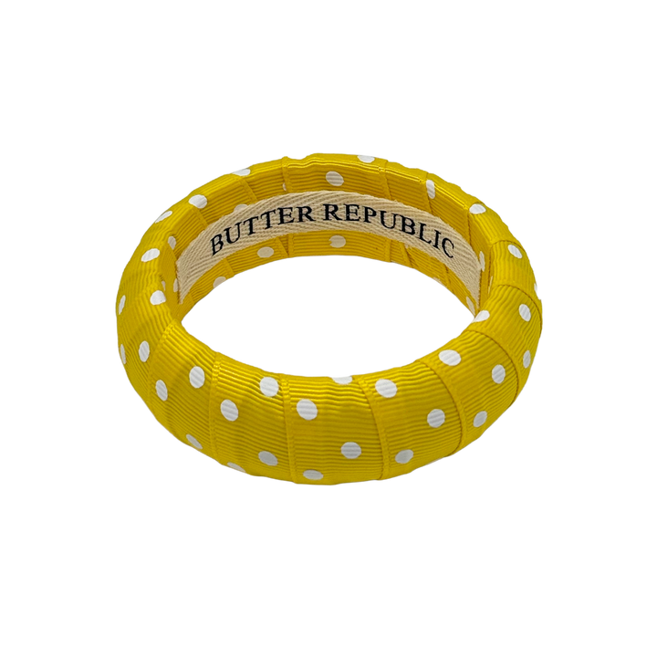 Yellow and white polka dot bangle bracelet with Butter Republic brand label on the interior